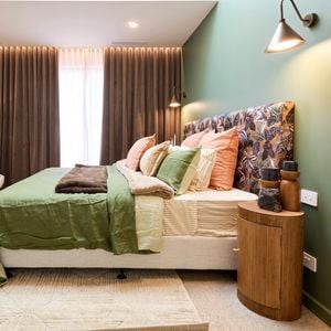 Bedroom with green feature wall, patterned headboard, and layered bedding.