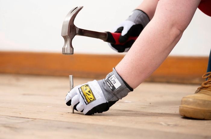 A close-up of a person using a hammer to fix nails in a timber floor, making it ready for cleaning and sanding.
