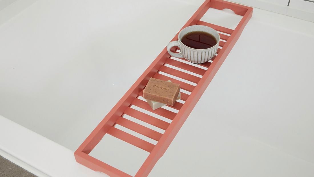 Painted bath caddy over bathtub with soaps and coffee cup.