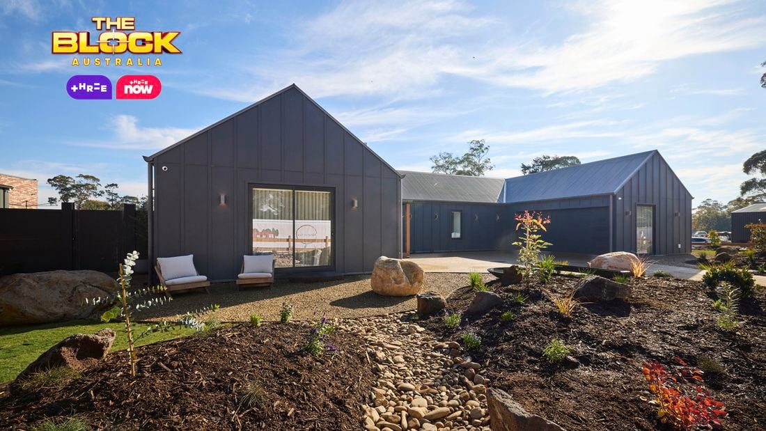 The front area of a house with rocks, shrubs, a driveway and a timber fence in it.