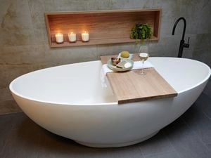 A free-standing bath with a timber shelf holding food and a glass of wine