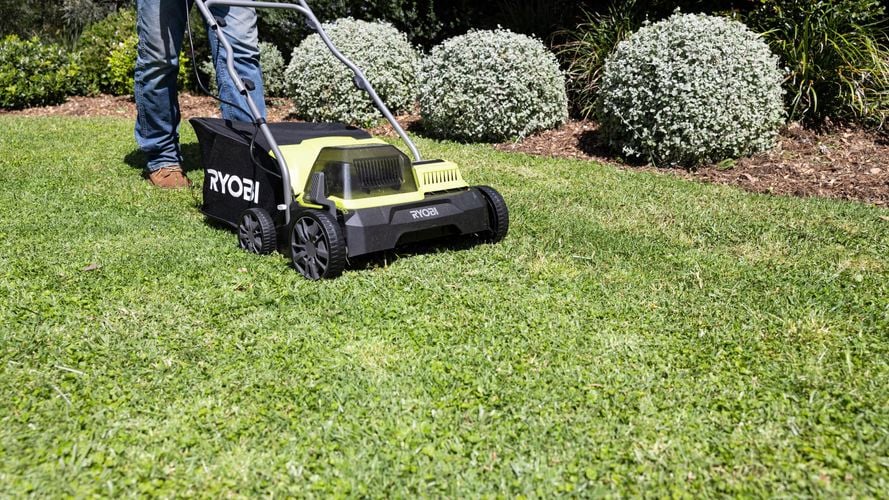 A person operating a lawn mower to cut the grass on a garden. 