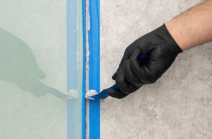 ​A person is smoothing freshly applied silicone sealant using a smoothing tool to create a clean, even and professional-looking finish.
