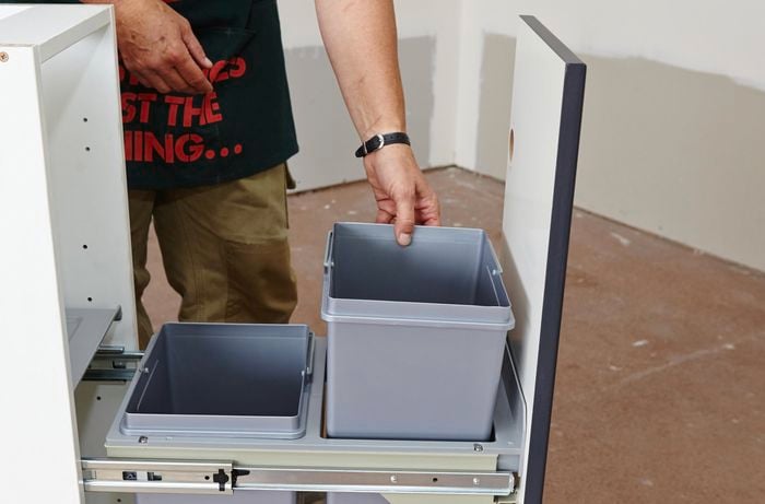 A person inserting square bins into a frame on runners