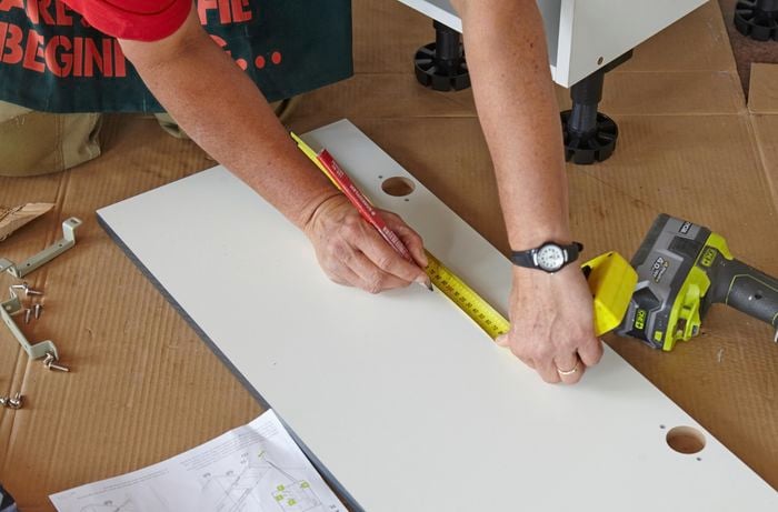 A person marking hole positions on inside of a cabinet panel 
