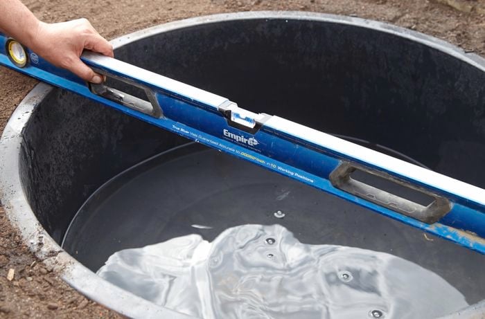 A person placing a spirit level across a plastic pond inserted in the ground