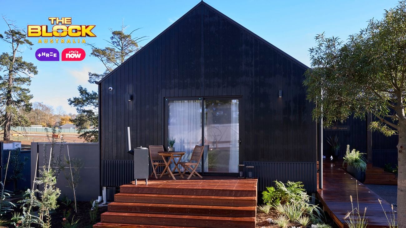 The front of a house with steps out the front of a room, a grassed area and trees in it.
