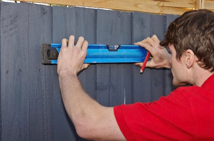 A Bunnings team member using a spirit level to mark a the clothesline position on the fence.