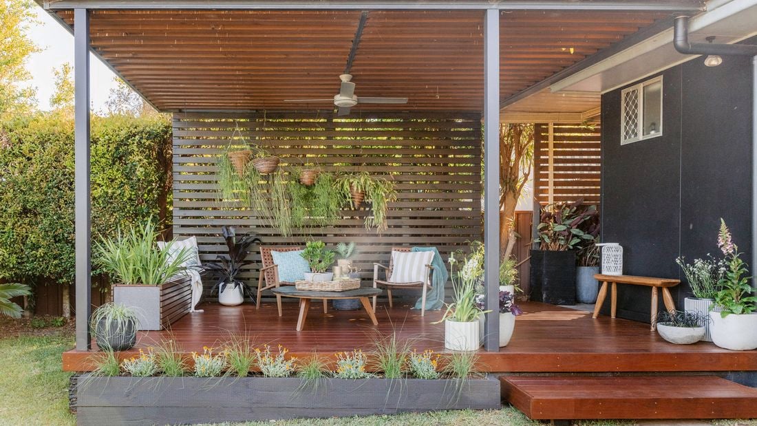 Outdoor entertaining area with timber deck, potted greenery, and hanging plants beneath a covered roof