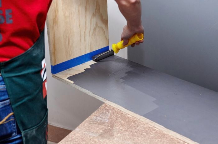 A person painting the inside face of a timber shelving unit using a mini roller