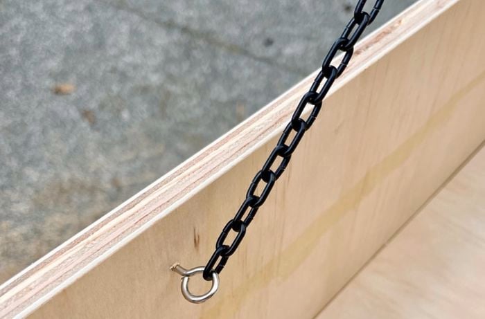 A wooden box with an eye hook attached to the side, with a black length of chain threaded through it