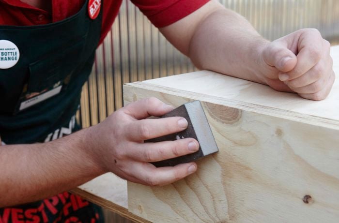 A person sanding a sheet of plywood using an sanding block