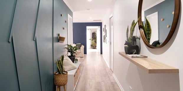 Hallway with green wall, floating shelf, mirror and side table.