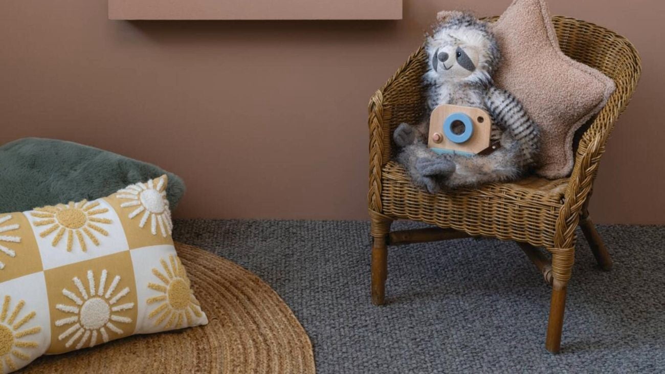 Brown painted wall with scallop shelves filled with children’s picture books. A chair and a rug with cushions sits beneath