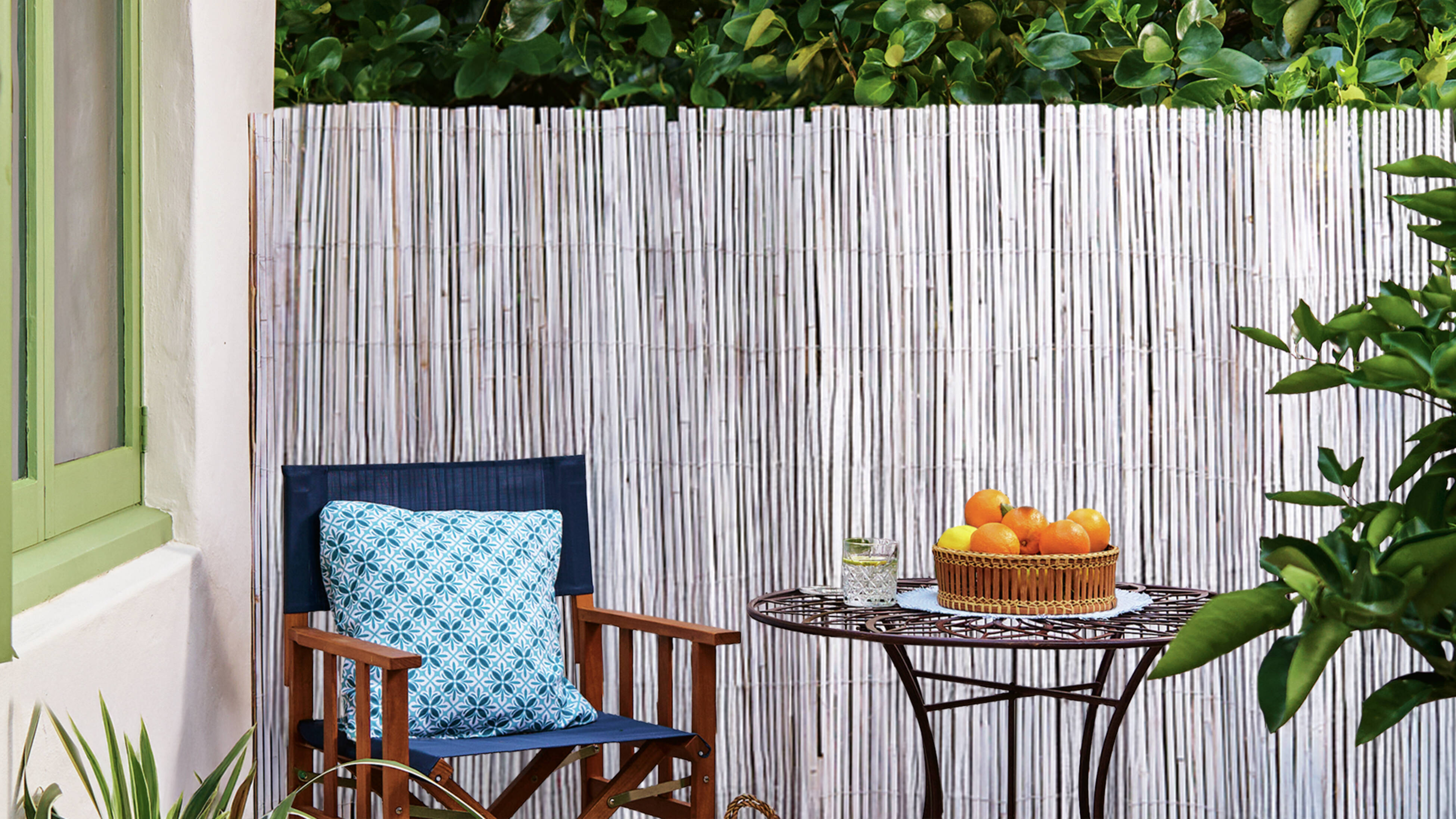 A timber director’s chair and bistro outdoor table sit in front of an upcycled bamboo screen.