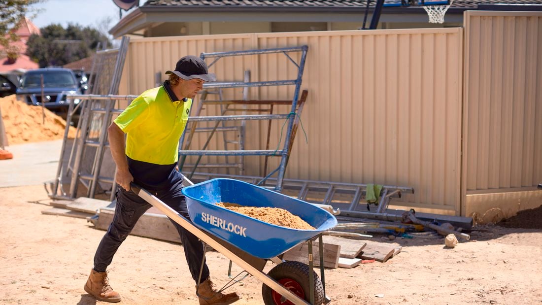 A man in hi-vis wheels a wheelbarrow full of soil on a building site