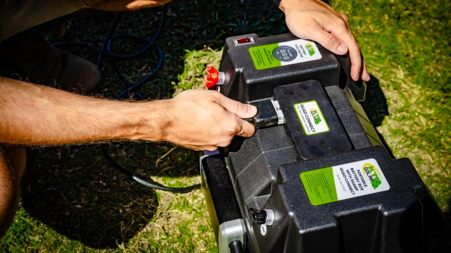 Person connecting a KT Solar Portable Battery Box Quad-Connect power system outdoors.