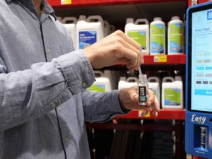 Customer testing pool water using a test strip beside a Hy-Clor digital water testing station in a Bunnings store.