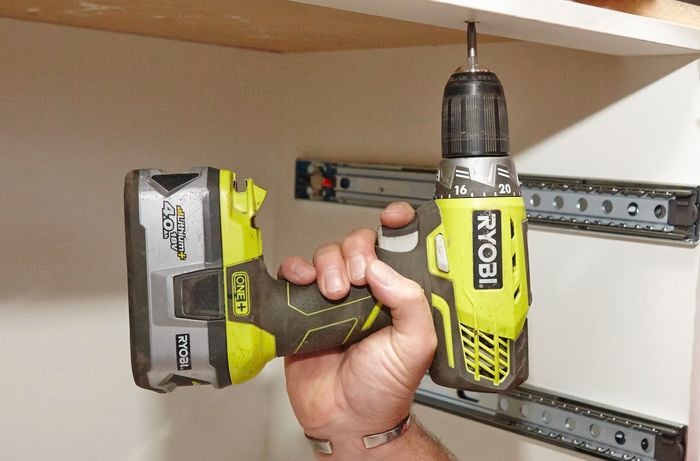 A person screwing into a cabinet from underneath with a cordless driver