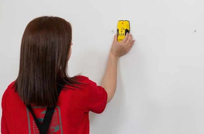 Person using a stud finder on a plaster wall