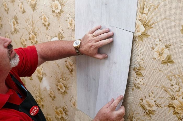 Faux wooden panels being applied over a wallpapered wall