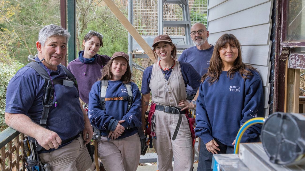 Team of six people, four young women in construction and two older men, on a building site]