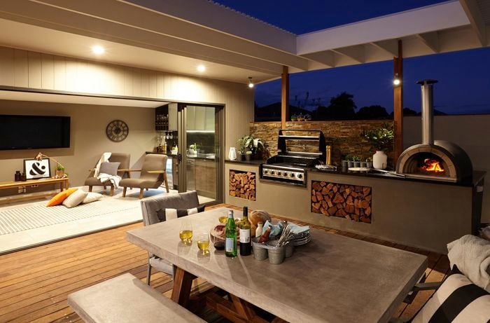 An outdoor room with wood-fired pizza oven, BBQ and furniture looking into a living room
