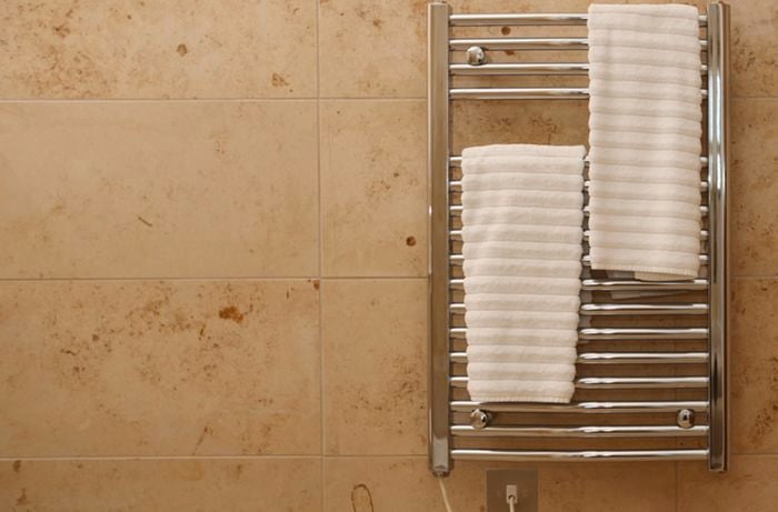 Towel rail with two white towels hanging from it, against a tile wall
