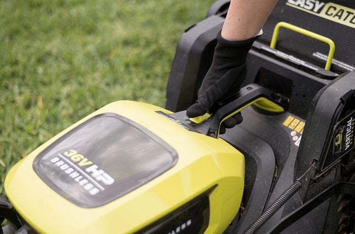 Ryobi lawn mower with person's thumb on the start button.