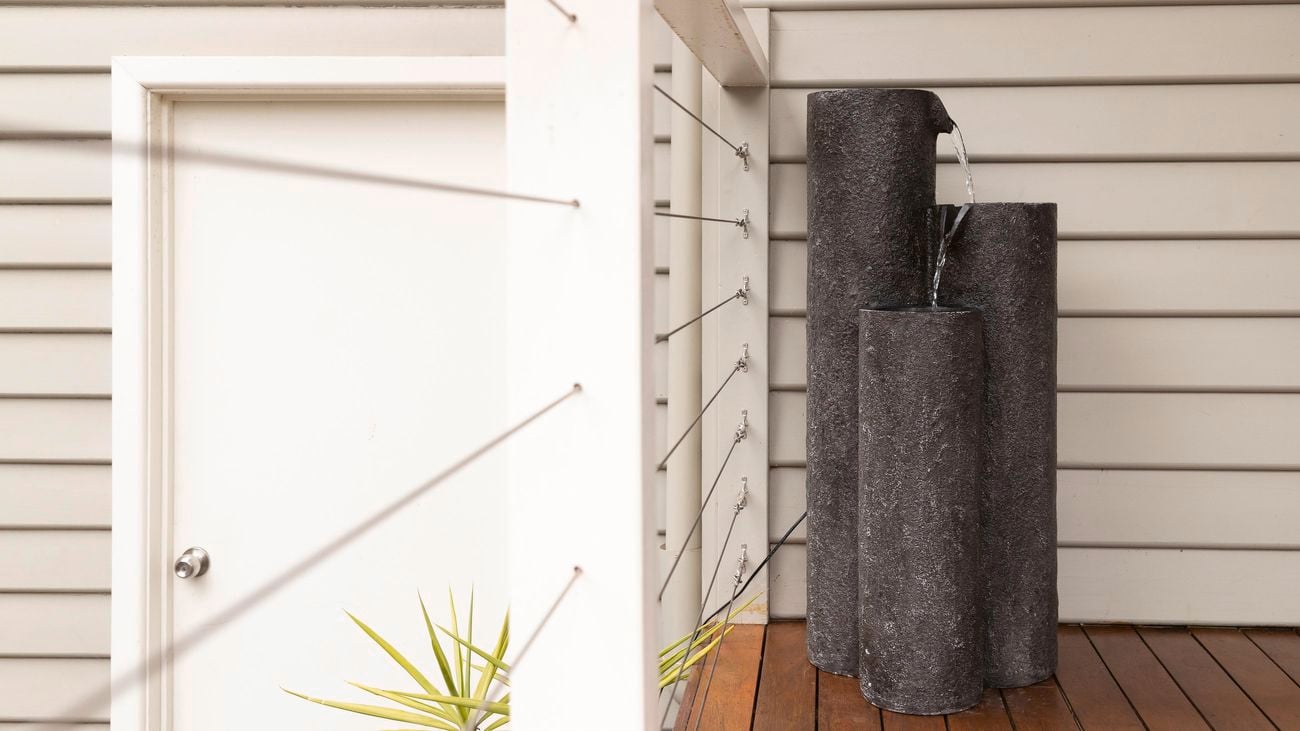 Tuscan Path three pillar black water feature on a deck with pale weatherboard background