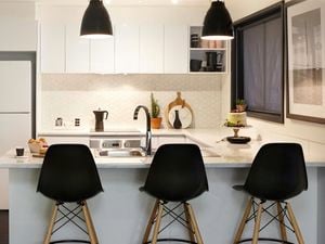 A Kaboodle kitchen with a white benchtop and cabinets, black stools and black pendant lights.
