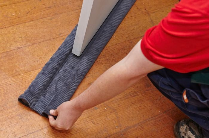 A person sliding a double snake underneath a door