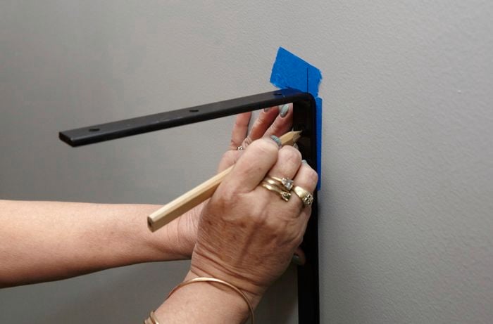 A person marking the hole position for an angle bracket on a wall