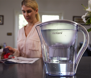 Water filter jug filled with water on a bench with a woman reading in the background