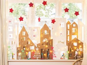 A Christmas window display featuring a homemade cardboard Advent calendar village on the sill, framed by waterfall lights and red craft stars.]
