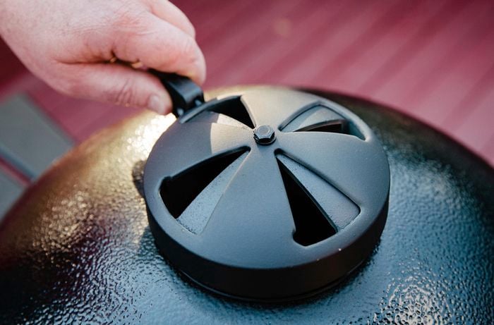 Person adjusting the intake vent on a kamado smoker