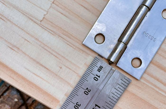 A panel of wood with a metal ruler and a hinge placed on top