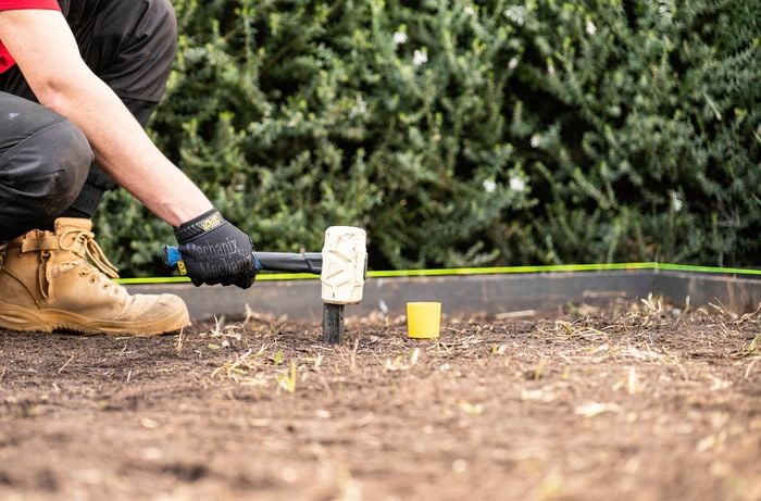 A person wearing gloves and work boots is placing pegs in the centre of the area to prepare for compacting. 