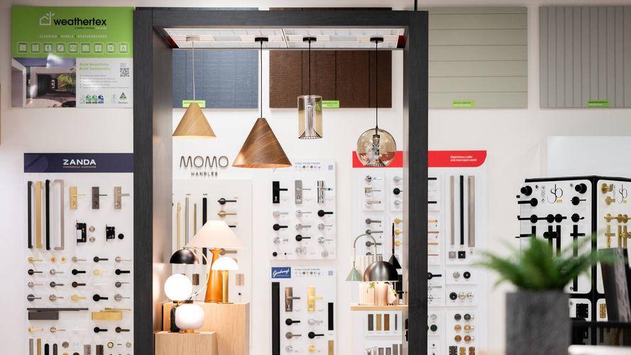 Building products and hardware showroom featuring decorative lighting displays, door hardware sample boards and wall cladding selections.