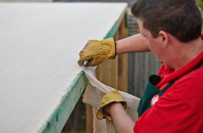 Excess shade cloth being trimmed from a wooden frame by a Bunnings team member on a ladder