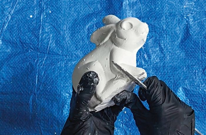 Person using the back of a butter knife to smooth out any bumps or blemishes on the plaster of paris bunny.