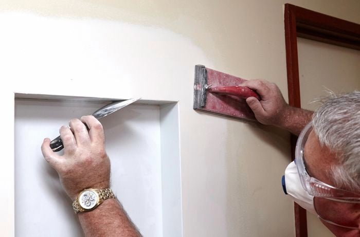 A person using a scraper to smooth the edge of a wall niche