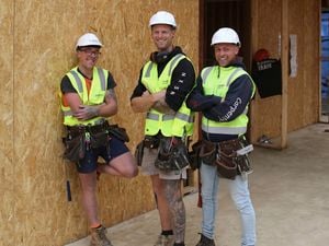 Three tradies standing in front of chipboard and wearing hat hats have a laugh on a job site