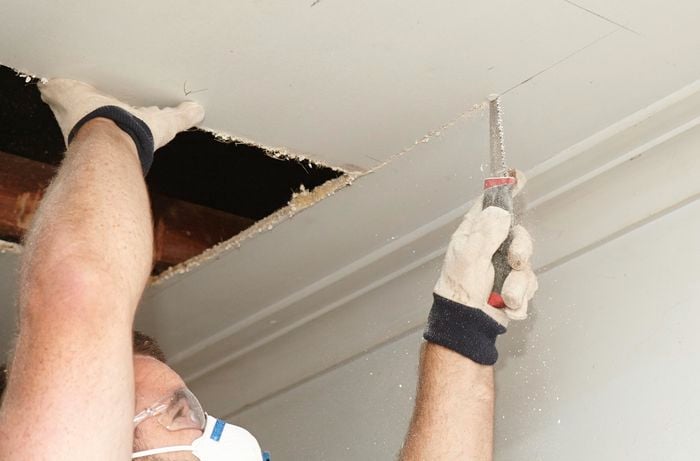 A person cutting a hole in a ceiling using a plaster saw