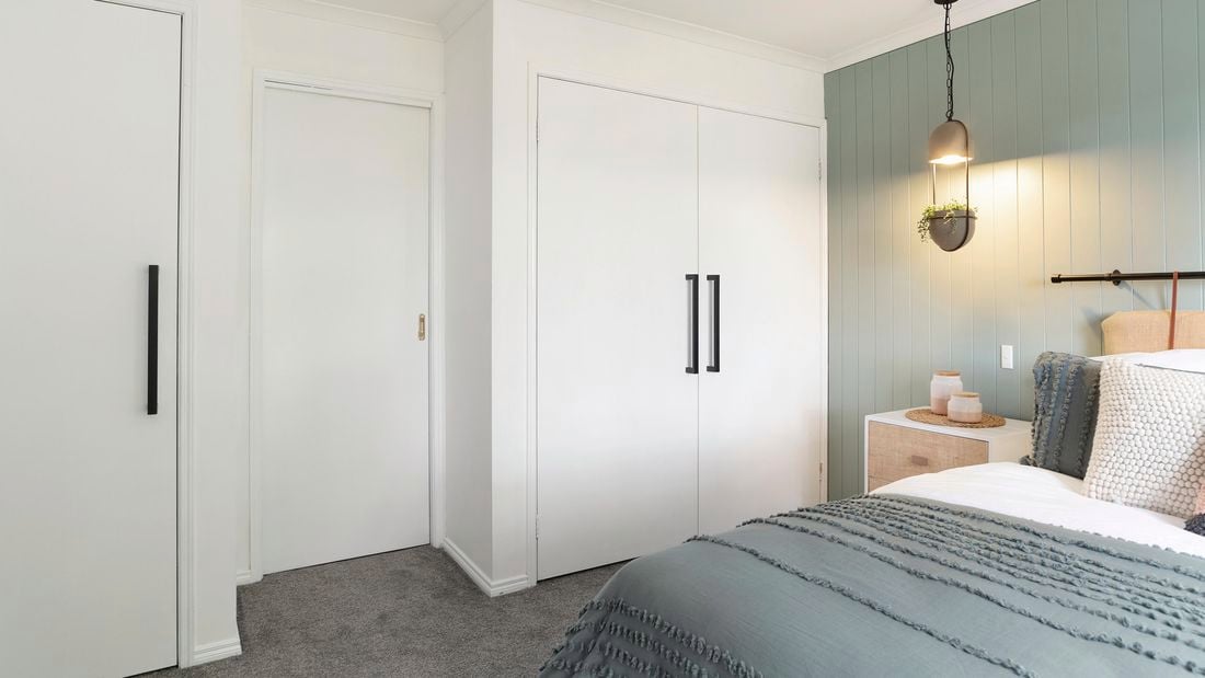 A bedroom with white built-in wardrobes with large black handles