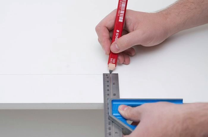 A person uses a ruler and red carpenter's pencil to mark a vertical line on the edge on the side opposite the lugs. 