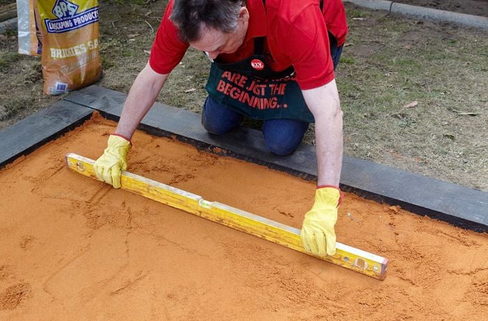 A person using a spirit level to level a bed of sand