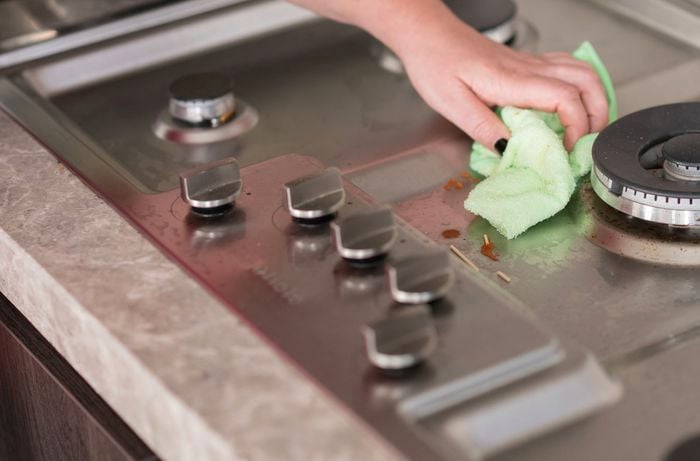 A hand is wiping the gas cooktop with a microfiber cloth.