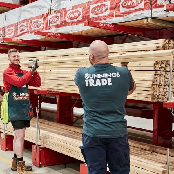 Two Bunnings team members lifting lengths of timber in the timber yard