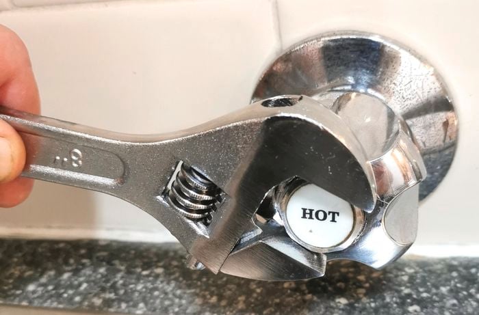 A silver wrench unscrewing a silver tap at a bathroom sink.